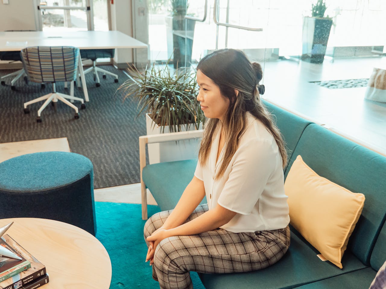impact-img Asian woman in a modern office setting, sitting on a sofa for a meeting.